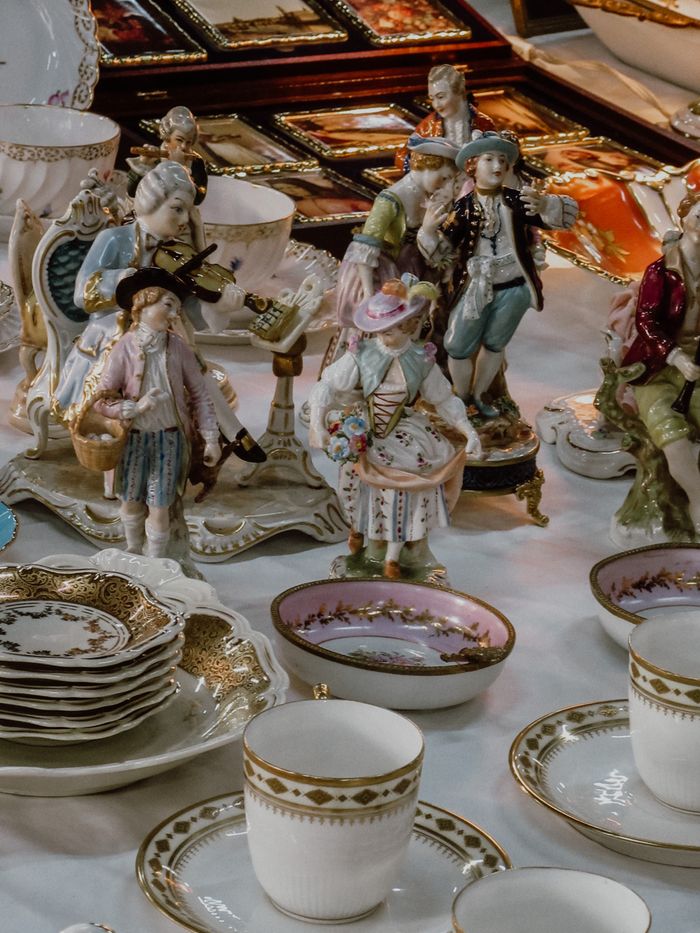 A collection of ornate antique figurines with elegant teacups and plates in a close-up vertical shot.
