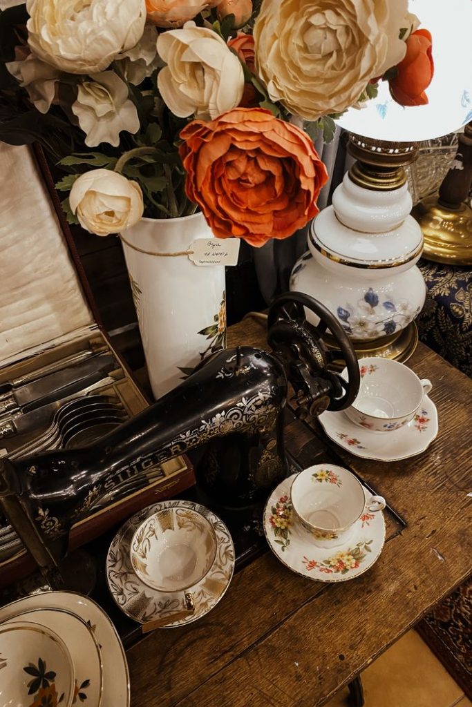 A cozy vintage setup with a sewing machine, floral arrangements, and tea cups on a wooden table.